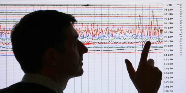 A seismologist poses for the media as he points to a seismographic graph showing the magnitude of the earthquake in Japan, on a monitor at the British Geological Survey office in Edinburgh, Scotland March 11, 2011. The biggest earthquake on record to hit Japan struck the northeast coast on Friday, triggering a 10-metre tsunami that swept away everything in its path, including houses, ships, cars and farm buildings.    REUTERS/David Moir (BRITAIN - Tags: DISASTER ENVIRONMENT) - RTR2JR7P
